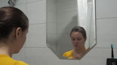 Banyoda yüz yıkama köpüğü kullanan genç bir kadın. Her yaşta günlük cilt bakımı ve kendine bakım kavramı.