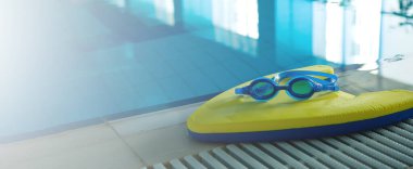 Spor merkezinde yüzme havuzunun yanında gözlüklerle yüzme tahtası. Yüzme eğitimi konsepti. Metin için afiş kopyalama alanı.