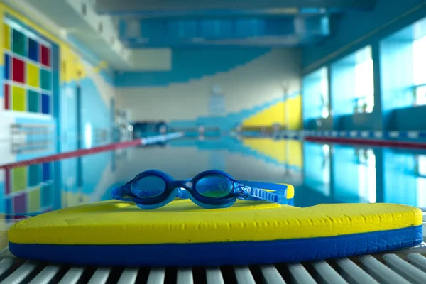 スポーツセンターのスイミングプールの横にあるゴーグルでボードを泳ぐ。水泳トレーニングの概念です。テキストのコピースペース. — ストック写真