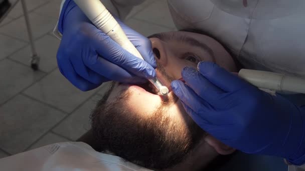 Γυναίκα επαγγελματίας οδοντίατρος εφαρμόζει μια ειδική πάστα στα δόντια ενός ασθενούς σε μια οδοντιατρική κλινική. Υγιεινή φροντίδα της στοματικής κοιλότητας. Προληπτικός καθαρισμός δοντιών σε στοματολογική κλινική. — Αρχείο Βίντεο