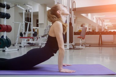Spor salonundaki antrenmandan önce spor paspası üzerinde ısınmak için esneyen atletik bir kadın. Vücuduna odaklanmış ve dikkatli ol.