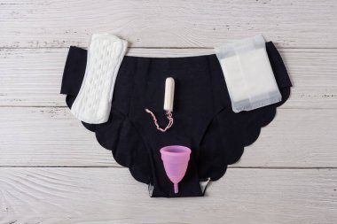 Farklı türde kadınsı adet hijyen ürünleri, pedler, pedler, tamponlar ve iç çamaşırlı bardaklar. Beyaz tahta arkaplan.