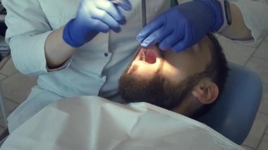 Kadın dişçi, dişçi aletinin yardımıyla hastanın ağız boşluğunu yakından inceliyor. Koruyucu diş hijyeni ve kontrol.