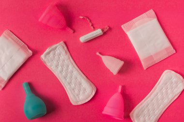 Kadınsı adet hijyen ürünlerinin farklı türleri. Pedler, pedler, tamponlar ve fincanlar gibi. Pembe arkaplan.