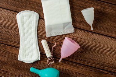 Kadınsı adet hijyen ürünlerinin farklı türleri. Pedler, pedler, tamponlar ve fincanlar gibi. tahta arkaplan. 