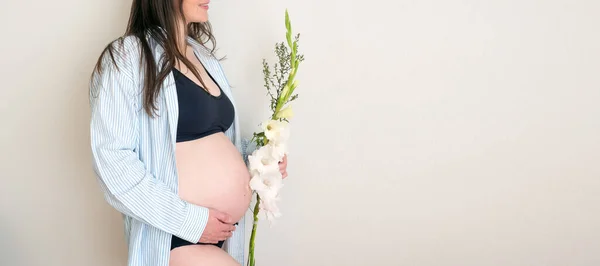 Vista laterale autentico relax donna incinta con fiore in camicia con grande pancia nuda. gravidanza sana. — Foto Stock