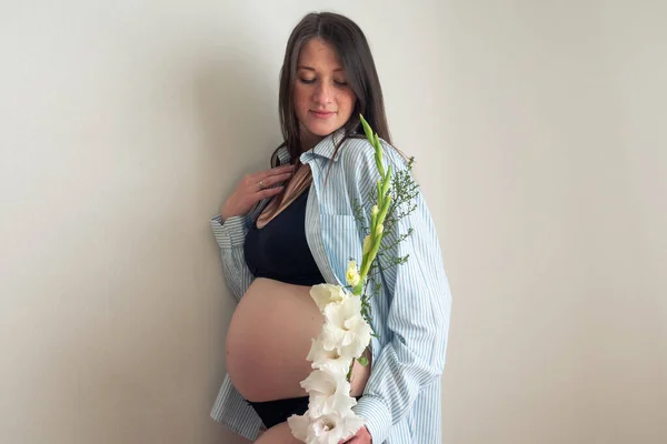 Vista laterale autentico relax donna incinta con fiore in camicia con grande pancia nuda. gravidanza sana. — Foto Stock
