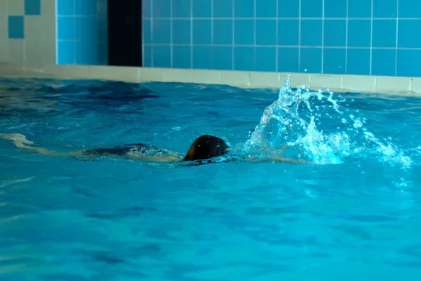 Onherkenbaar kind zwemmen freestyle stijl training in zwemmer zwembad met spetterend water. Stockfoto