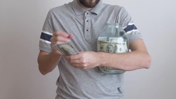 Un hombre sosteniendo un frasco grande de vidrio y poniendo billetes de dinero en ella. dinero concepto de ahorro. consumo moderado y economía. — Vídeos de Stock