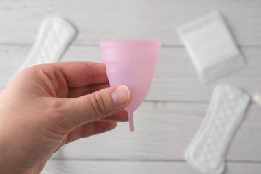 Adet bardağı ellerinde. Ahşap arka planda alternatif kadın adet hijyen ürünleri.