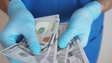 Erkek tıp doktoru el ele tutuşup onları sayarak yüz dolarlık banknotları tutuyor. Kırmızı bölgedeki çalışanlara yapılan ödemeler. Ödül