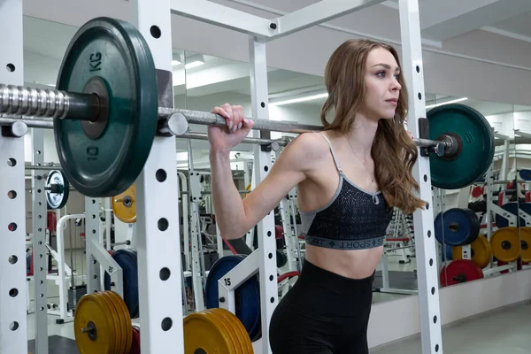 Sporty woman preparing to lift heavy weights while working out alone in a gym. Side view close up of concentrated fitnesswoman with long hair. — Zdjęcie stockowe