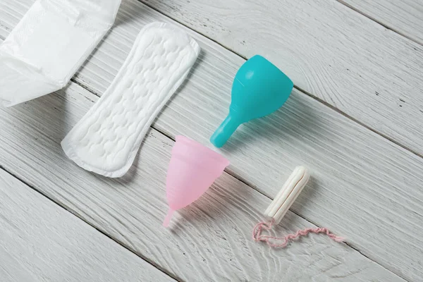 Different types of feminine menstrual hygiene materials products such as pads cloths tampons and cups. White wooden background. — Stock Photo, Image