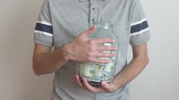 Un hombre sosteniendo un frasco de vidrio grande con dinero y acariciándola. dinero concepto de ahorro. consumo moderado y economía. — Vídeos de Stock