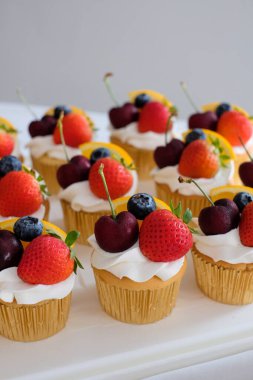 Butter cupcakes topped with strawberries, oranges and blueberries. Homemade bakery concept.