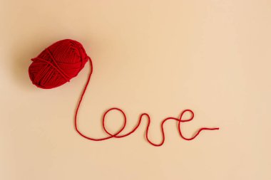Red yarn with love text on orange pastel background. Happy valentine concept.
