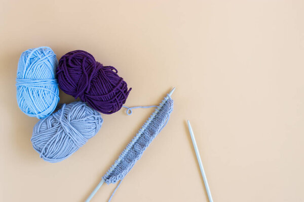 Top view of gray knitting wool and knitting needles on pastel orange background.