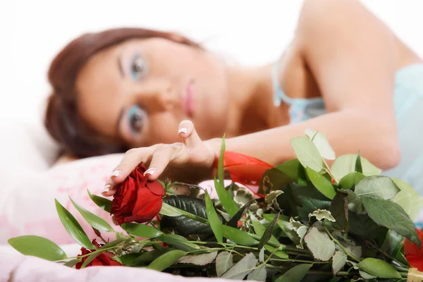 Hermosa mujer sexy acostada en la cama en lencería sosteniendo rosas rojas —  Fotos de Stock