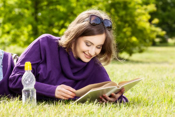 Mujer feliz leyendo libro acostado en la hierba —  Fotos de Stock