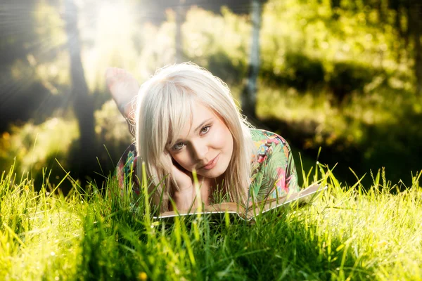 Menina encontra-se na grama verde e lê livro — Fotografia de Stock