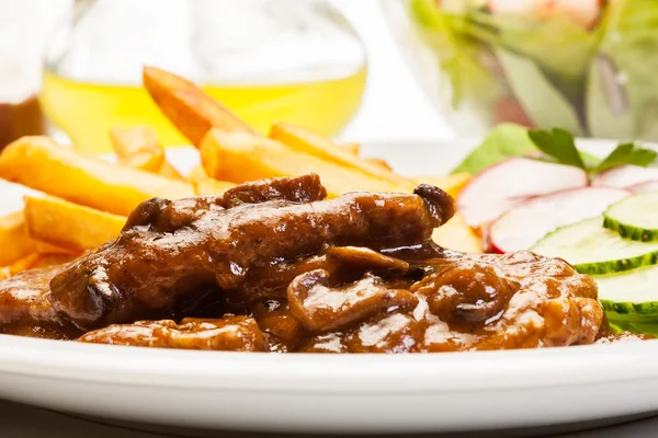 Costeleta de porco com molho, cogumelos e batatas fritas — Fotografia de Stock