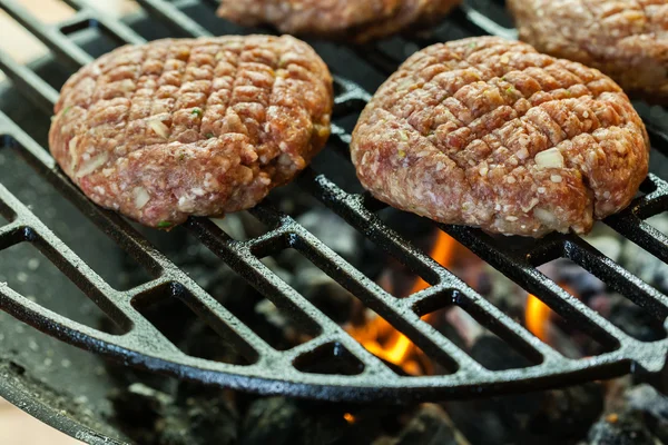 Hamburguesas crudas en parrilla barbacoa con fuego —  Fotos de Stock