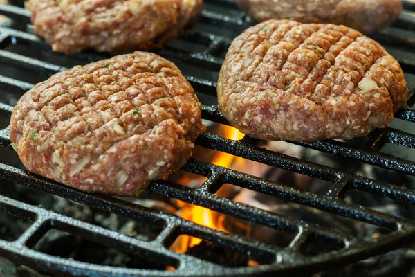 Hamburguesas crudas en parrilla barbacoa con fuego —  Fotos de Stock