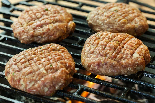 Raw burgers on barbecue grill with fire — Stock Photo, Image