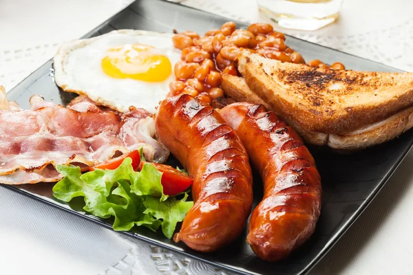 Englisches Frühstück mit Speck, Wurst, Ei, gebackenen Bohnen und Orangensaft — Stockfoto