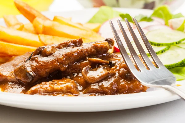 Costeleta de porco com molho, cogumelos e batatas fritas — Fotografia de Stock