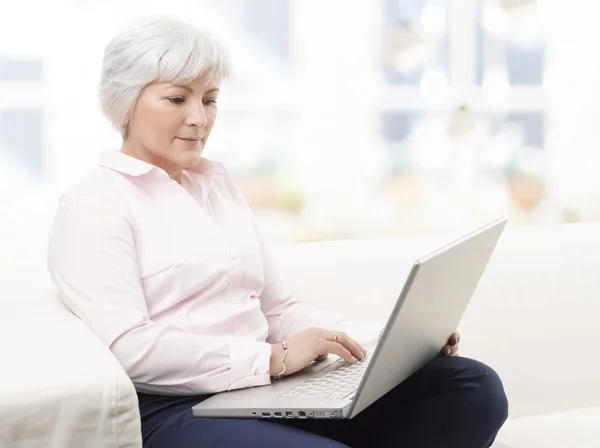 Leende senior kvinna som arbetar på bärbar dator — Stockfoto