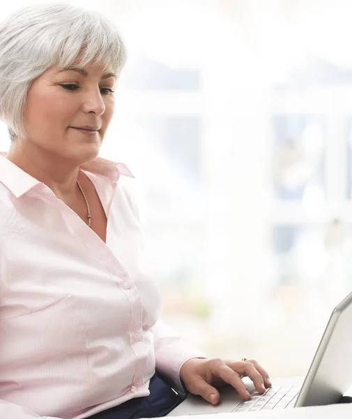 Uśmiechający się starszy kobieta pracuje na laptopie — Zdjęcie stockowe
