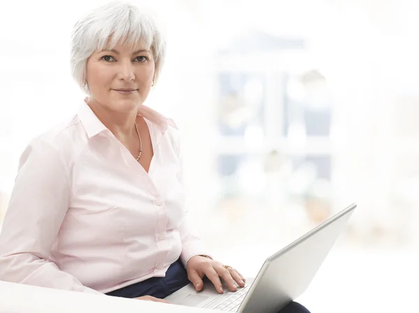 Lächelnde Seniorin arbeitet am Laptop — Stockfoto