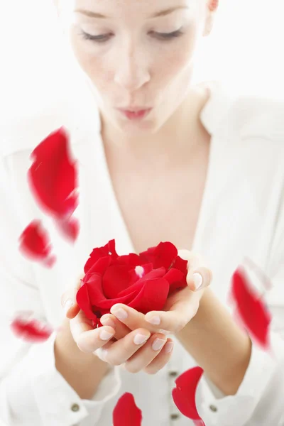 Beautiful, young woman blowing red rose petals from her palms — Stock Photo, Image