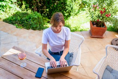Masada oturup bilgisayarını açık havada kullanan güzel bir kadının yüksek açılı görüntüsü..