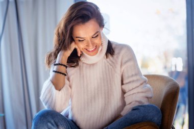 Evdeki koltukta dinlenirken gündelik giysiler giyen çekici bir kadın..