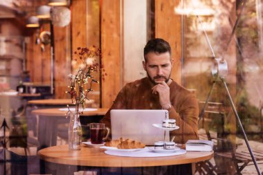 Kafede oturup dizüstü bilgisayarla çalışırken günlük kıyafetler giyen yakışıklı bir adam.. 