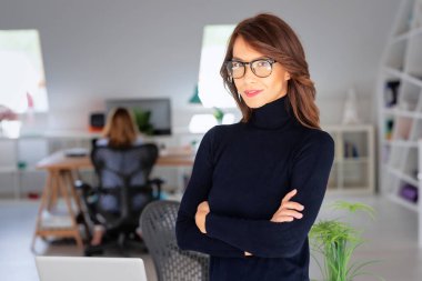 Confident middle aged businesswoman wearing turtleneck sweater while standing with arms crossed at office at the office.