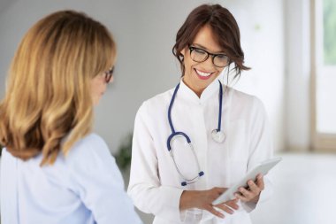 Female doctor standing on the corridor and using digital tablet while she is explaining her symptoms to the patient.