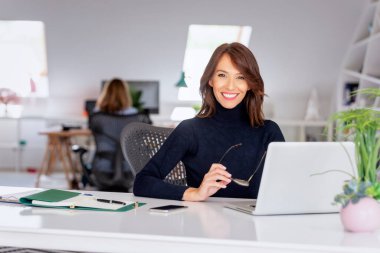 Kendine güveni tam orta yaşlı işkadını boğazlı kazak giyerken ofis masasında oturup yeni bir proje üzerinde çalışıyor.. 