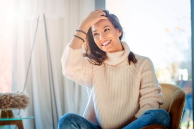 Shot of cheerful woman relaxing on the sofa at home. Attractive woman wearing casual clothes while sitting on the couch.