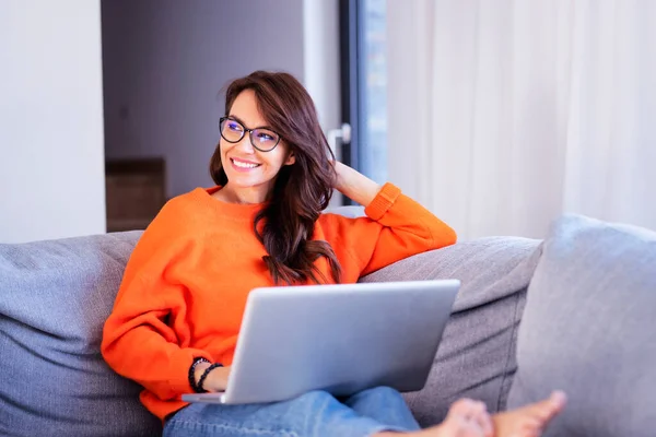 在家里坐在沙发上上网的时候用笔记本电脑射击快乐的女人 — 图库照片