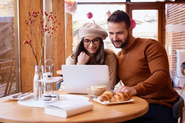 コーヒーショップに座っている間に 幸せな若い女性とハンサムな男のノートパソコンを使用してネット上で閲覧のショット — ストック写真