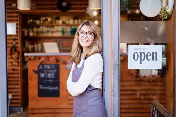 照片上 一位微笑的咖啡馆店主女商人抱着双臂站在门口等她的客人 在门上开标志 — 图库照片