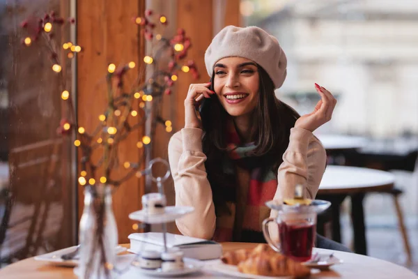 在咖啡馆里 她用手机拍了一张照片 拍的是一个快乐的年轻女人坐在桌子前与人交谈 — 图库照片