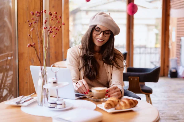 坎迪拍摄了一个快乐的年轻女子在咖啡店边吃早餐边在笔记本电脑上工作的情景 — 图库照片