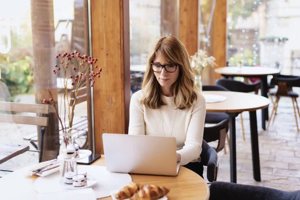 カフェの窓の近くに座っている間 ラップトップで働く自信を持って成熟した女性 中小企業 — ストック写真