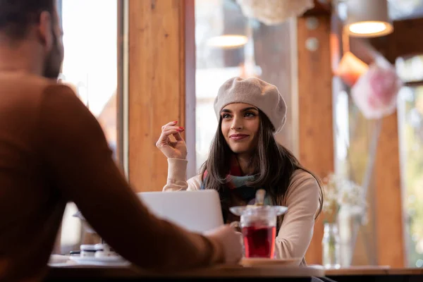 カフェで男とお茶を飲みながらテーブルに座っていると 美しい女性がベレー帽とスカーフを着ているのが見えた — ストック写真