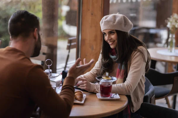 カフェで男とお茶を飲みながらテーブルに座っていると 美しい女性がベレー帽とスカーフを着ているのが見えた — ストック写真