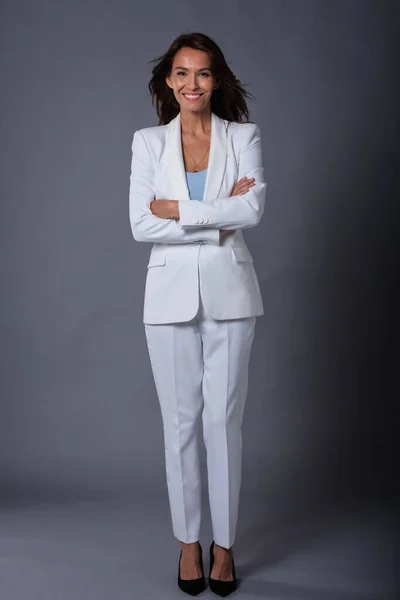 Gri Arka Planda Dikilirken Beyaz Takım Elbiseli Güzel Bir Kadın — Stok fotoğraf